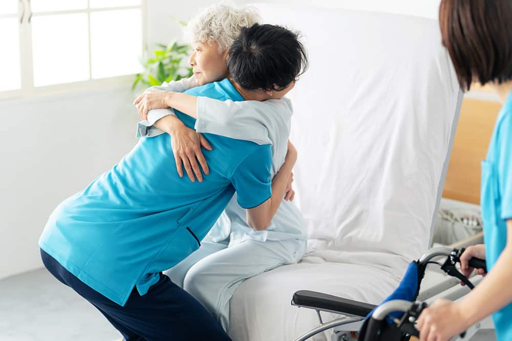 Elderly woman being transferred to a wheelchair from a bed 