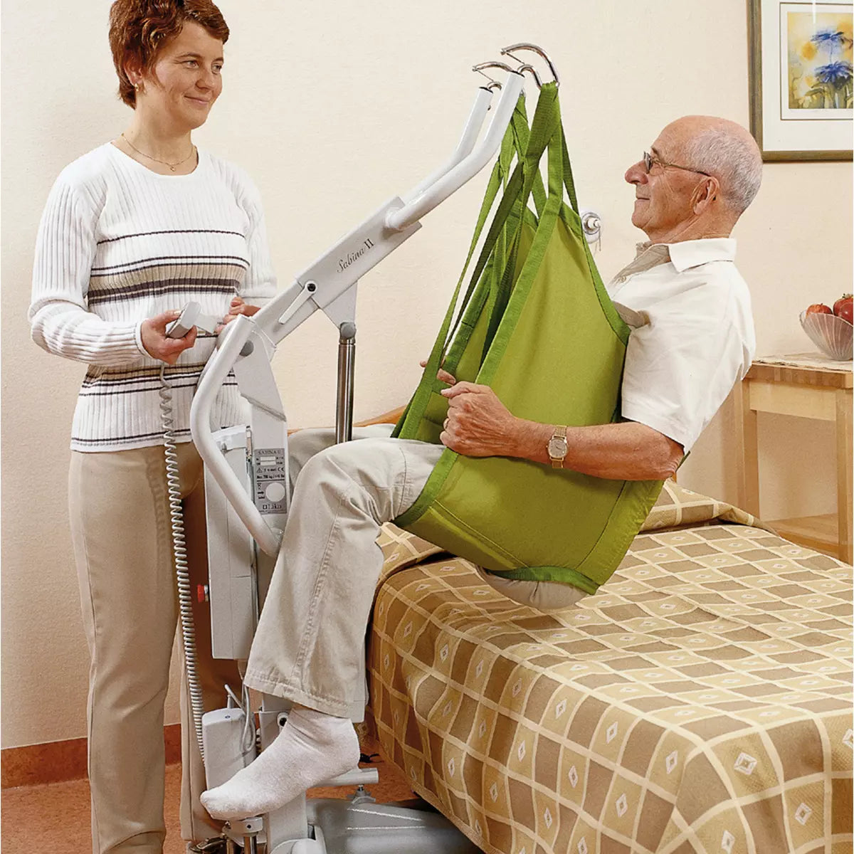 Hillrom M220 M230 Mobile Hoist in use to lift patient on a chair