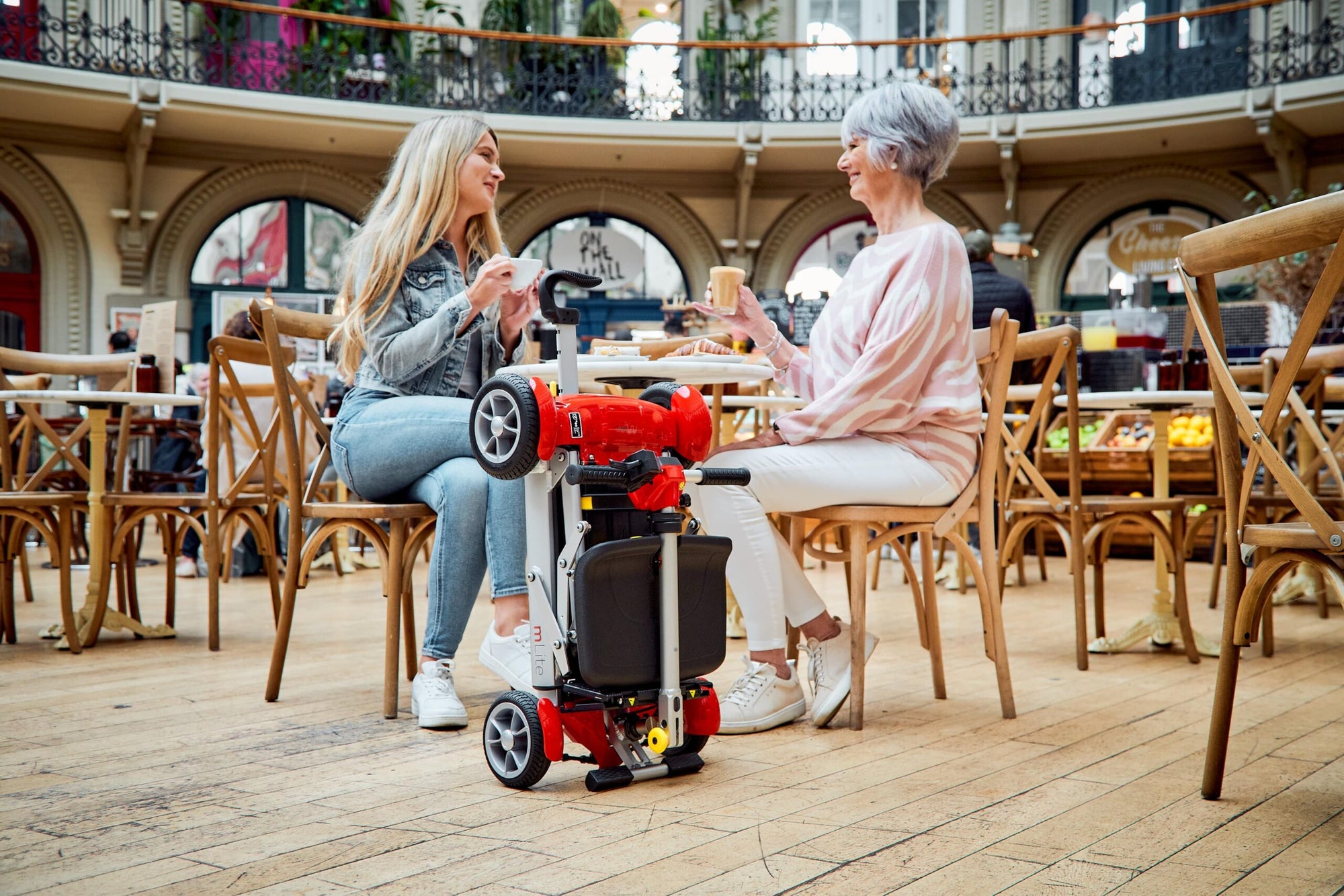 Motion Healthcare mLite Folding Mobility Scooter folded up beside owner in a cafe