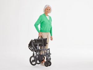 Woman carrying a folded Motion Healthcare Magnelite transit and self propelled, Lightweight, Folding Wheelchair, Manual and Self Propelled