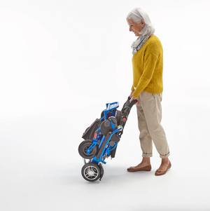 woman wheeling folded Motion Healthcare Foldalite Powerchair Lightweight, Electric Folding Wheelchair Lithium Battery