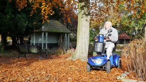 elderly man riding a Blue Scooterpac Ignite 8mph Electric Mobility Scooter 40 Mile Range in a park
